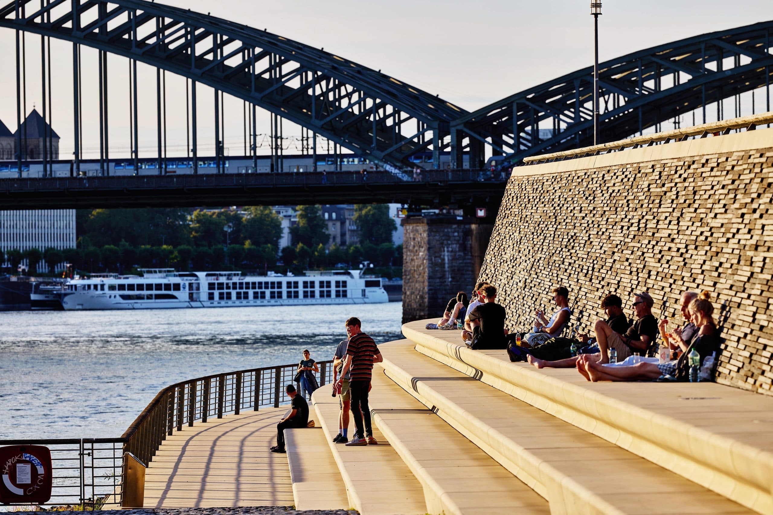 Belebte Sitzstufen am Rheinboulevard mit Blick auf die Brücke